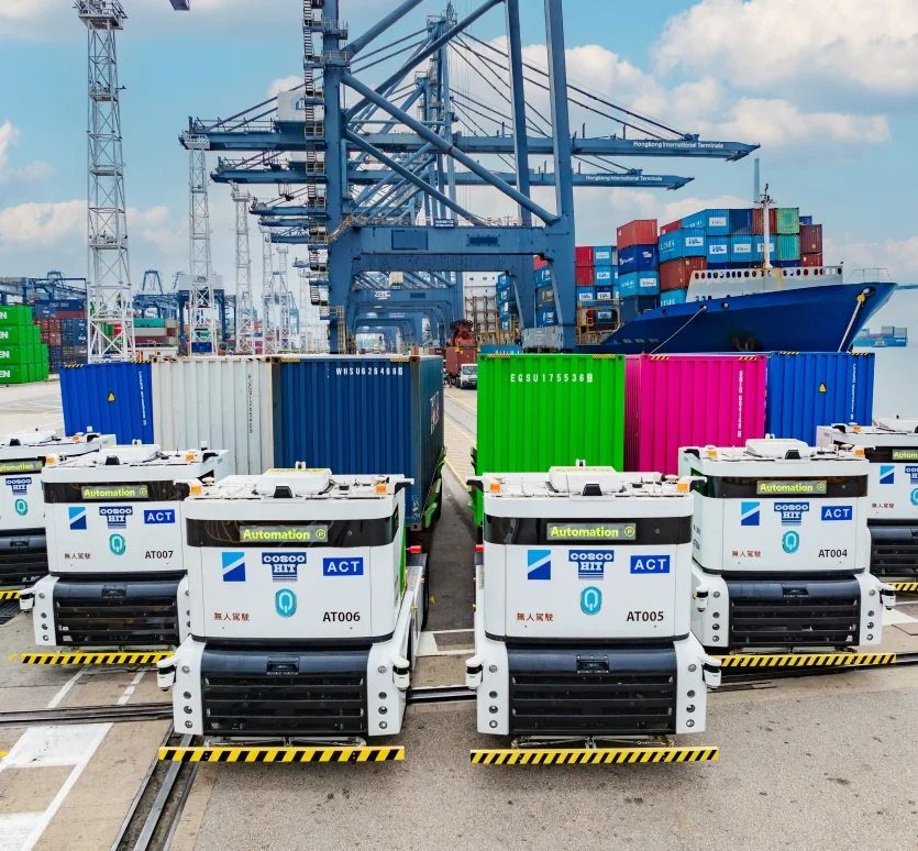 A fleet of Westwell Q-Truck autonomous prime movers lined up under the quay cranes at a container terminal